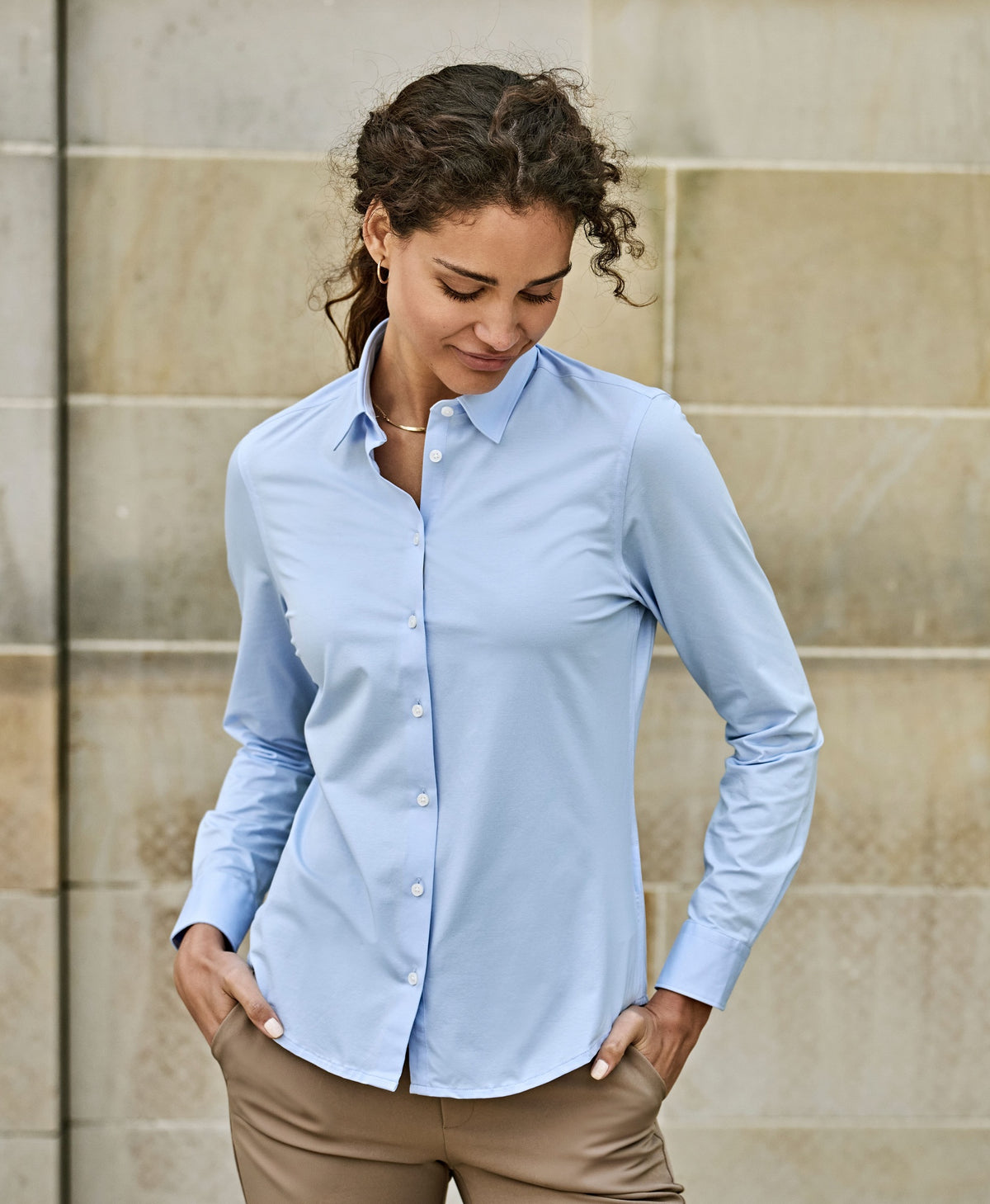 Woman wearing the Tee Jays Ladies Active Stretch Shirt in Light Blue, standing by a stone wall