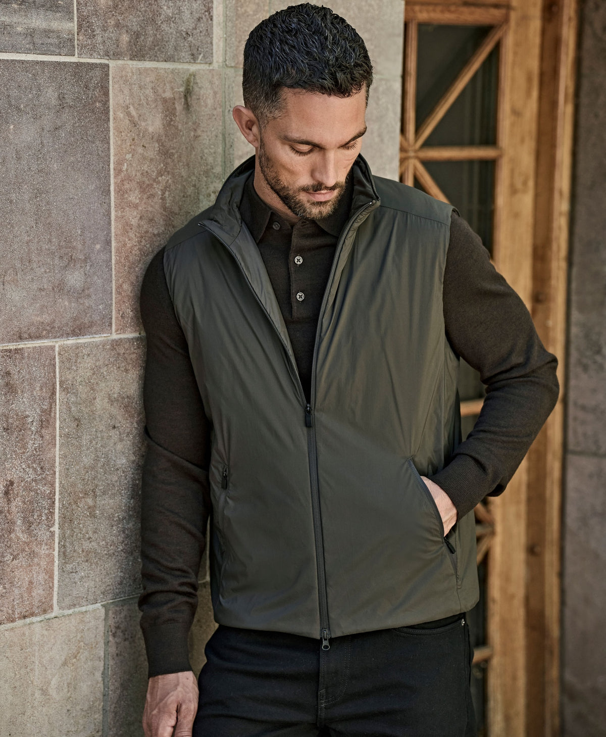Man wearing the Tee Jays Men’s PureLite Bodywarmer in Shadow, looking down by a stone wall
