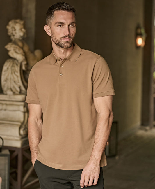 Man wearing the Tee Jays Men’s Luxury Stretch Polo Shirt in Wood, standing in a hallway