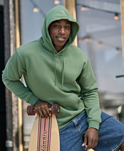 Man wearing the Tee Jays Unlabelled Hooded Sweatshirt Hoodie with the hood up, holding a skateboard