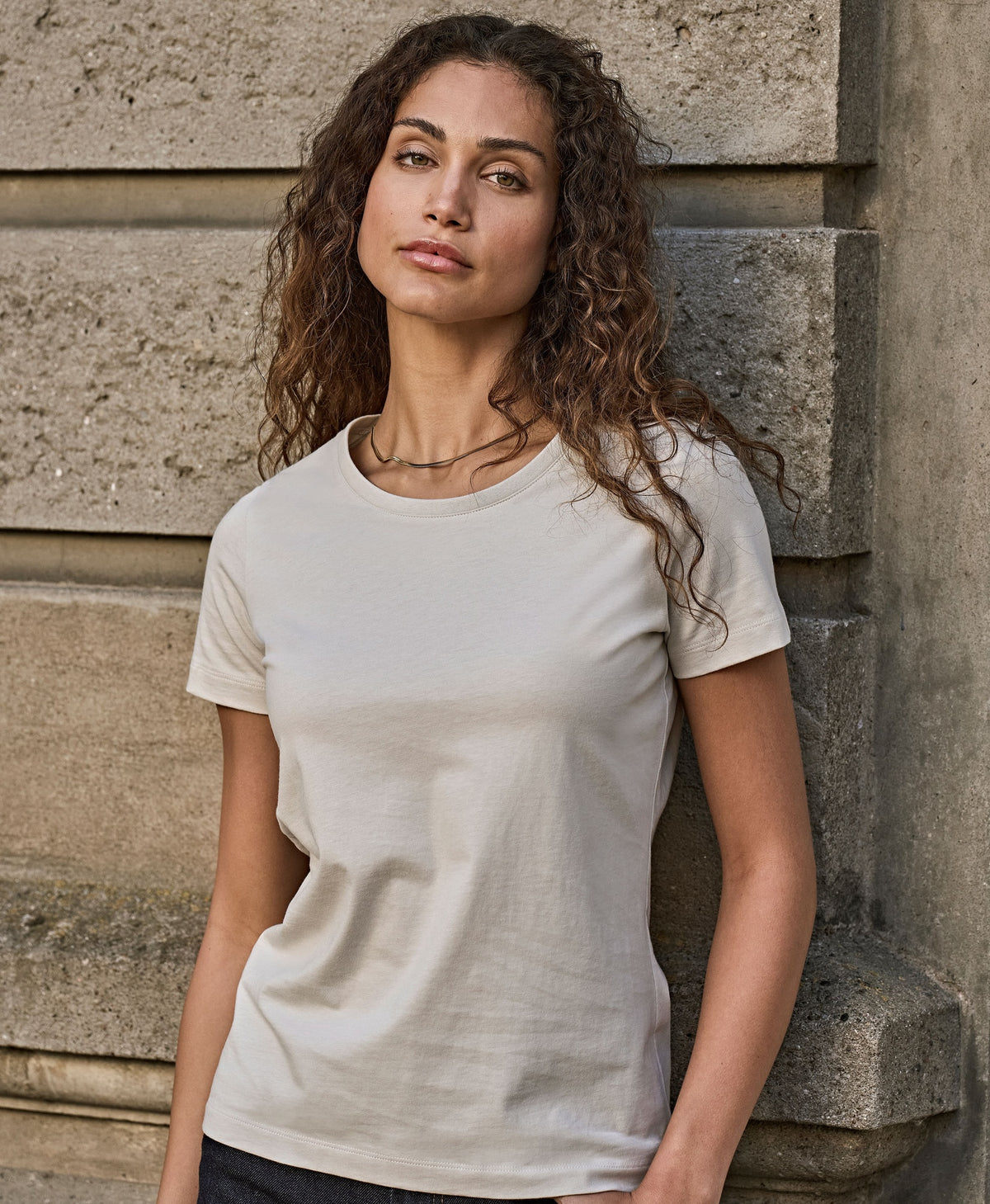 Woman wearing the Tee Jays Ladies Fashion Sof-Tee T-Shirt, standing by a stone wall