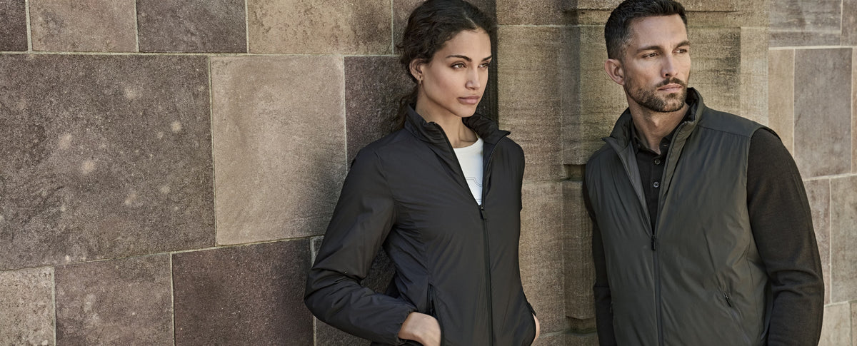 Woman wearing the Tee Jays Ladies PureLite Jacket beside a man, by a stone wall