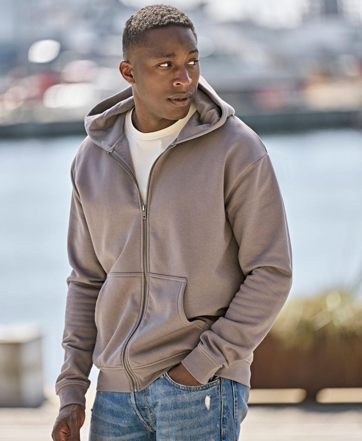Man wearing the Tee Jays Unlabelled Hooded Full Zip Sweatshirt Hoodie, standing by a harbour