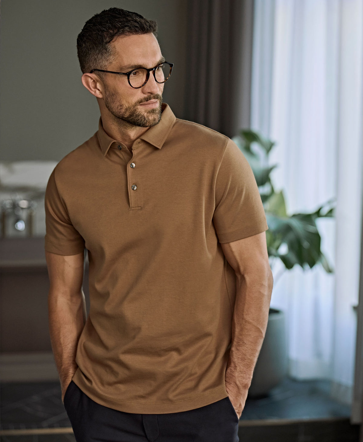 Man in glasses wearing the Tee Jays Men’s Pima Cotton Polo Shirt in Wood, standing by a window
