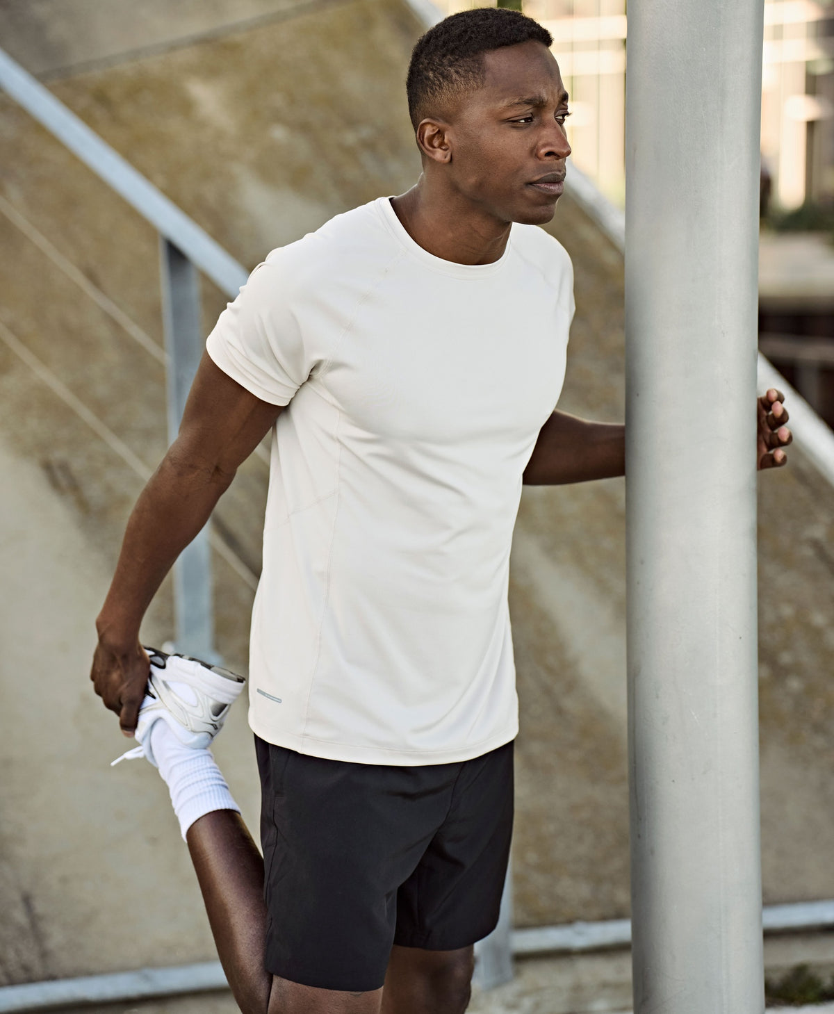 Man wearing the Tee Jays Men’s CoolDry T-Shirt, stretching by a lamp post