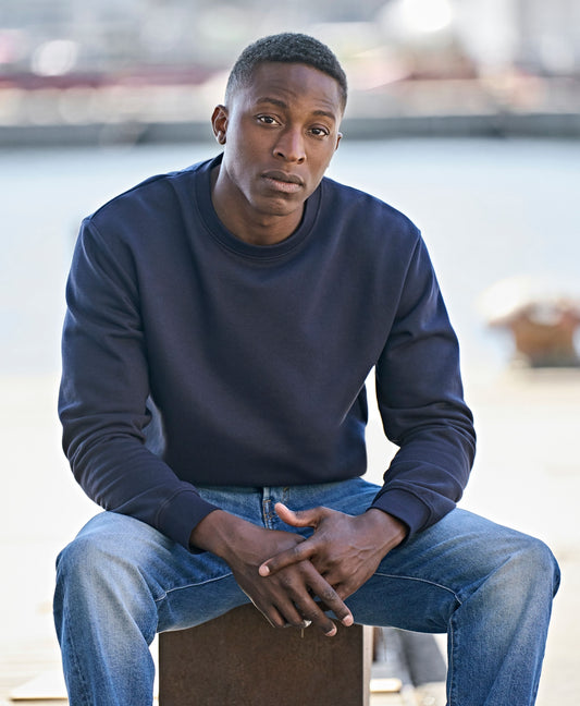 Man wearing the Tee Jays Unlabelled Sweatshirt in Navy, sitting by the water