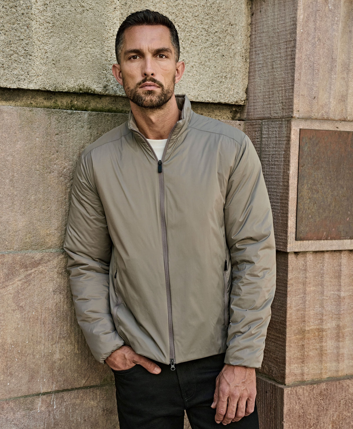 Man wearing the Tee Jays Men’s PureLite Jacket in Driftwood, standing by a stone wall