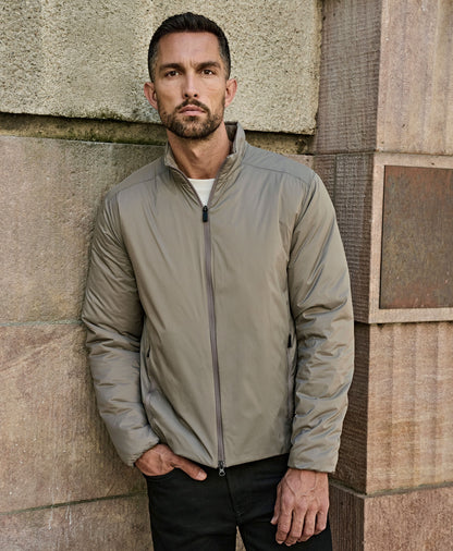 Man wearing the Tee Jays Men’s PureLite Jacket in Driftwood, standing by a stone wall