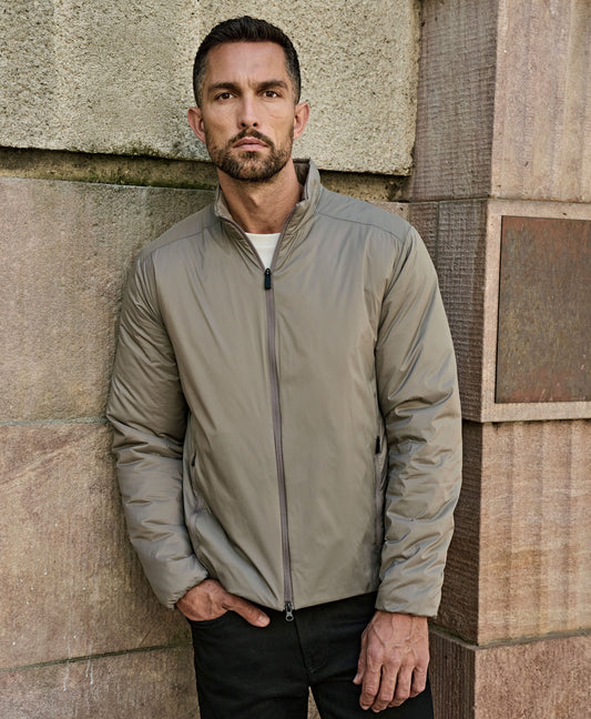 Man wearing the Tee Jays Men’s PureLite Jacket in Driftwood, standing by a stone wall
