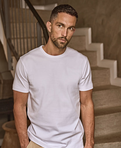 Man wearing the Tee Jays Men’s Interlock T-Shirt, standing on a stone staircase