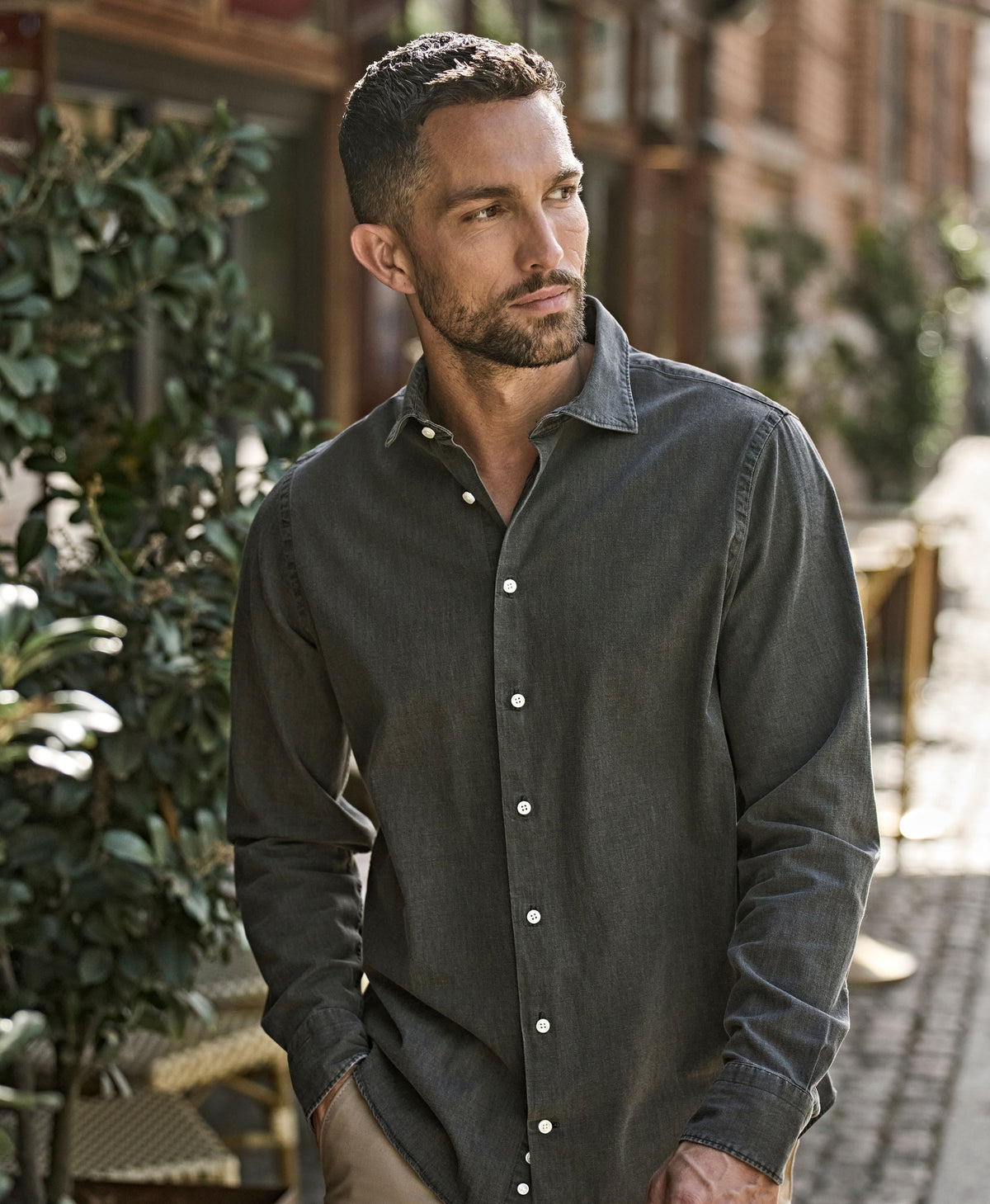 Man wearing the Tee Jays Men’s Denim Shirt in Black Denim, standing on a cobbled street