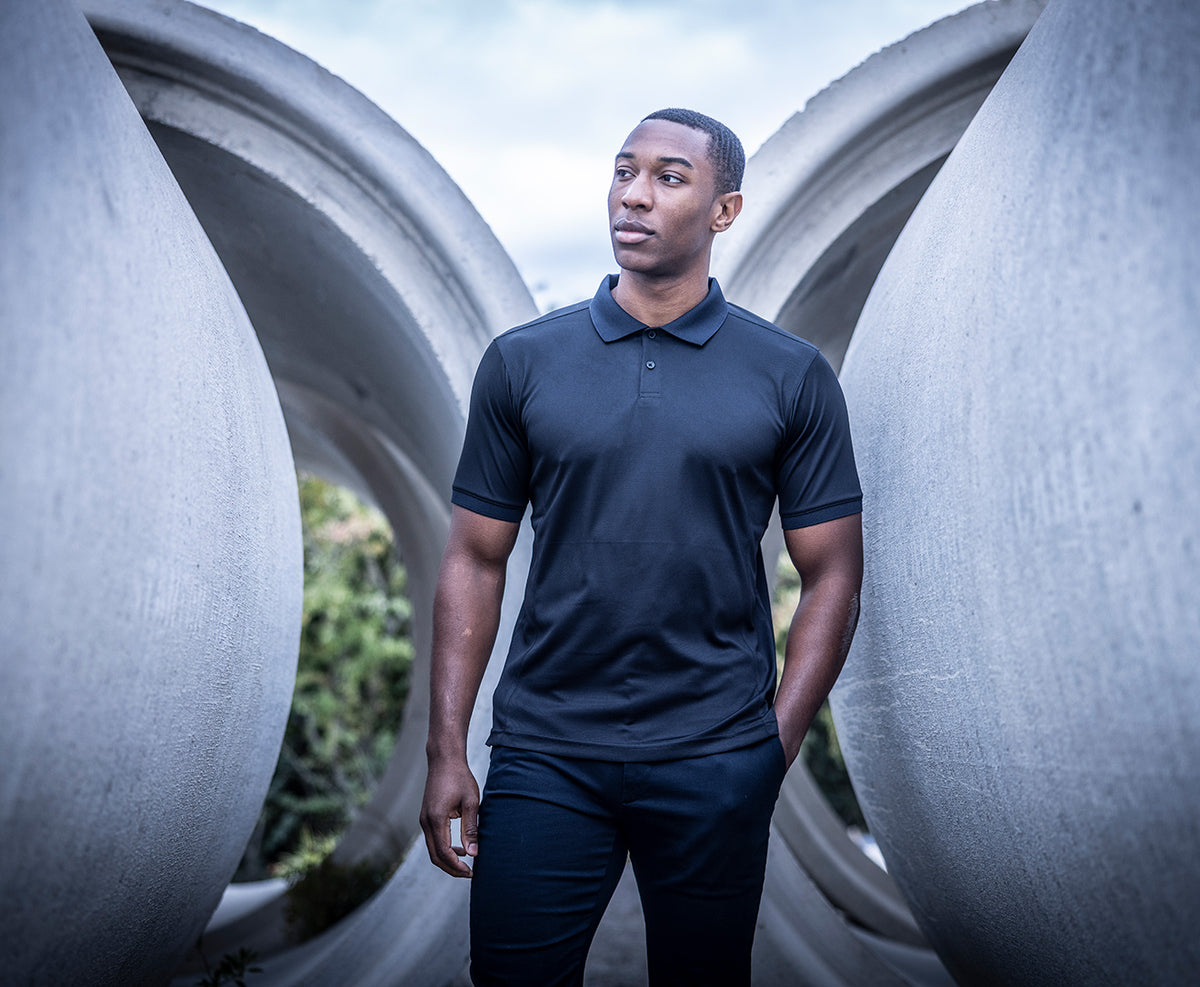 Man wearing the Regatta Recycle.Me Unisex Pique Polo Shirt, standing among large concrete pipes