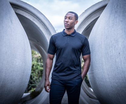 Man wearing the Regatta Recycle.Me Unisex Pique Polo Shirt, standing among large concrete pipes