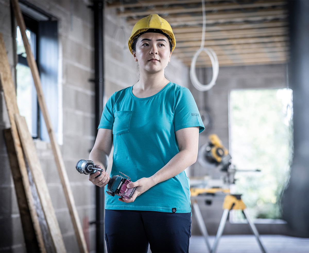 Woman in a hard hat wearing the Regatta Ada Ladies Cotton Stretch T-Shirt in Wilderness Green, holding a drill