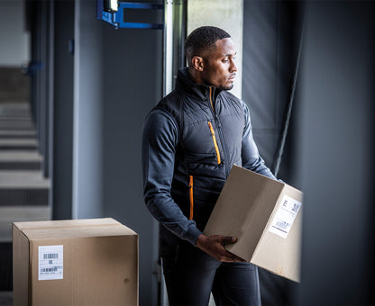 Man wearing the Regatta Pro Men’s Universal Bodywarmer in Black Orange Pop, carrying boxes through a doorway