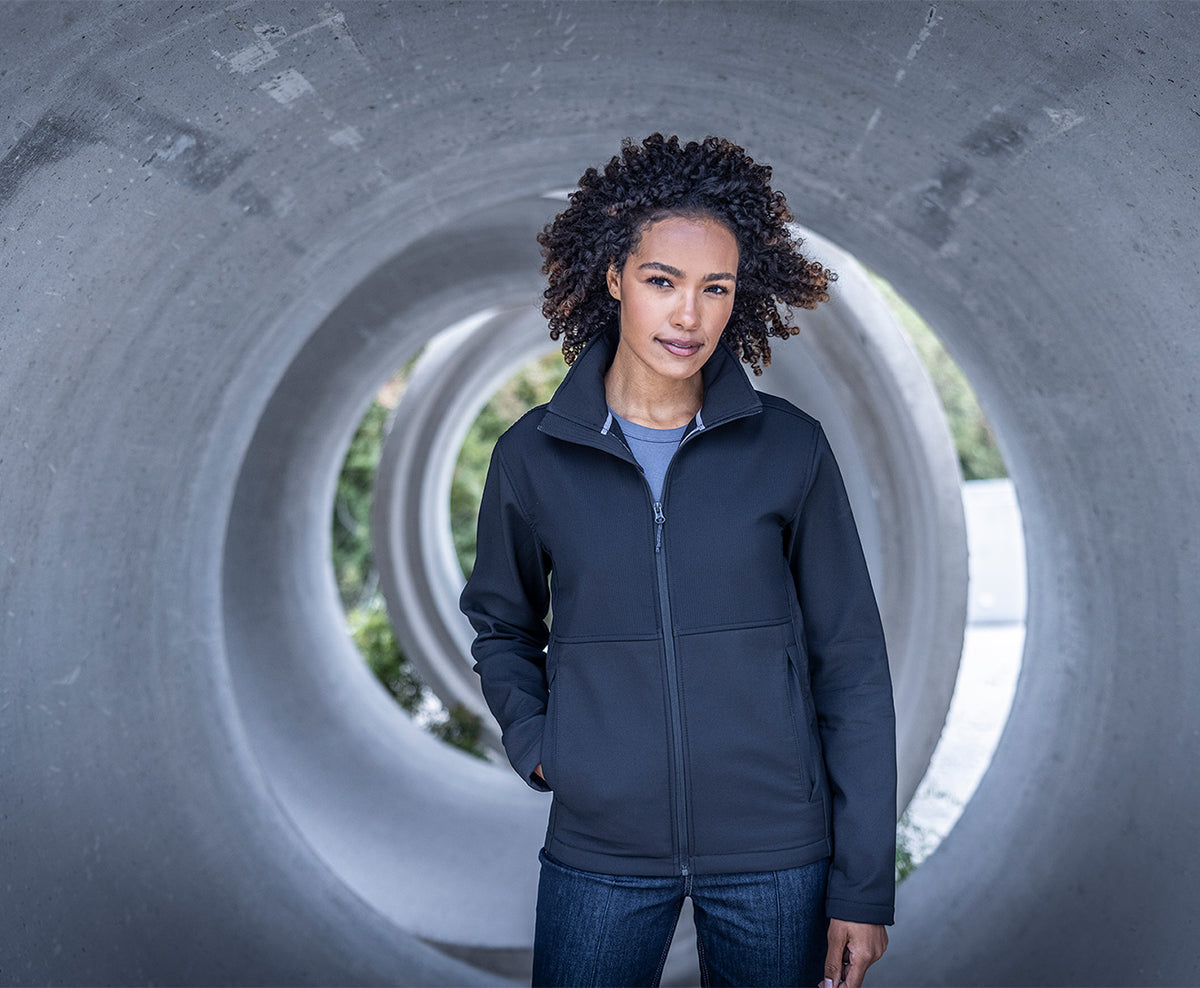 Woman wearing the Regatta Recycle.Me Unisex Softshell Jacket in Navy, standing in a concrete pipe