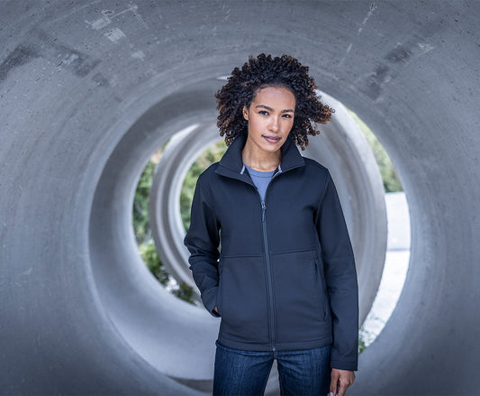 Woman wearing the Regatta Recycle.Me Unisex Softshell Jacket in Navy, standing in a concrete pipe