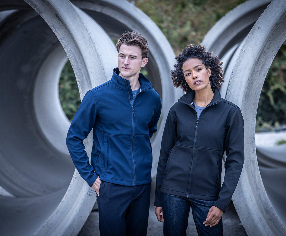 Man and woman wearing the Regatta Recycle.Me Unisex Softshell Jacket, standing among large concrete pipes