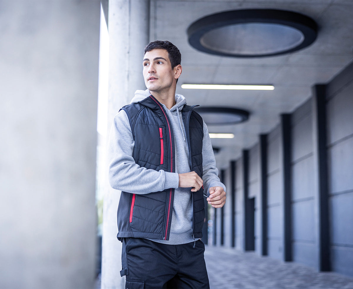 Man wearing the Regatta Pro Men’s Universal Bodywarmer in Black and Classic Red, walking along a corridor
