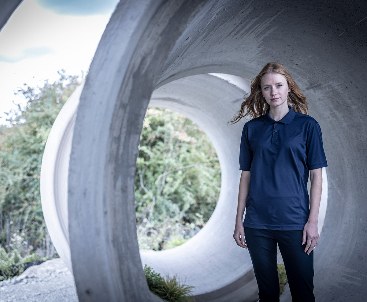 Woman wearing the Regatta Recycle.Me Unisex Pique Polo Shirt in Navy, standing in a concrete pipe