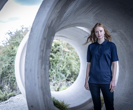 Woman wearing the Regatta Recycle.Me Unisex Pique Polo Shirt in Navy, standing in a concrete pipe