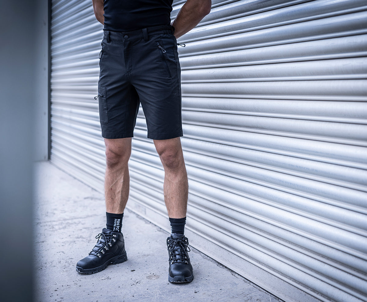 Man wearing the Regatta Prolite Men’s Stretch Shorts in Black, standing by a roller shutter