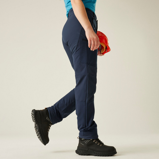 Model wearing the Regatta Prolite Ladies Stretch Trousers in Navy, side view, walking, holding a hard hat