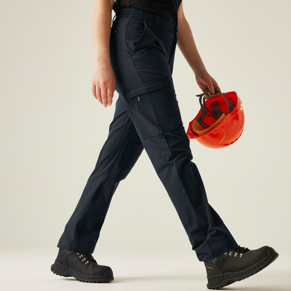 Model wearing the Regatta Pro Ladies Action Stretch Trousers in Navy, side view, walking, holding a hard hat