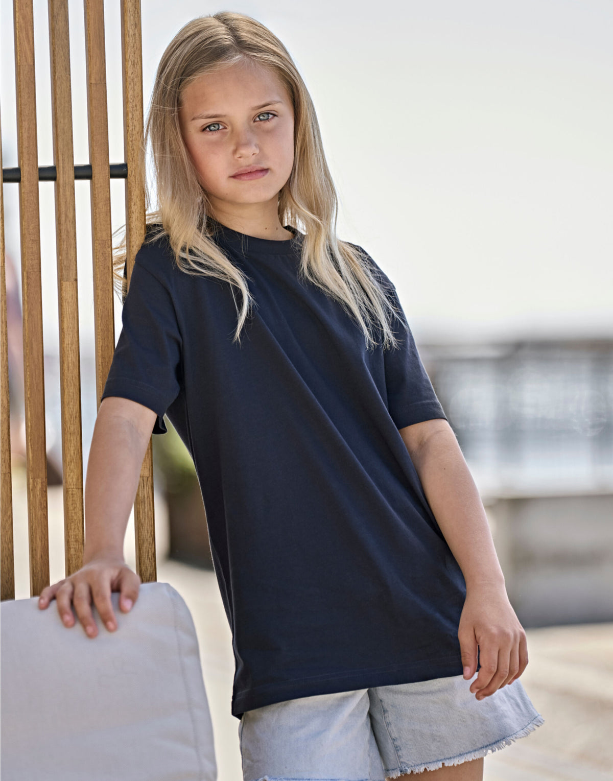 Girl wearing the Tee Jays Unlabelled Junior T-Shirt in Navy, leaning on a chair outdoors