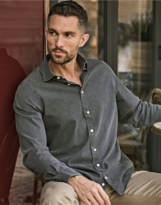 Man wearing the Tee Jays Men’s Denim Shirt in Black Denim, sitting by a doorway
