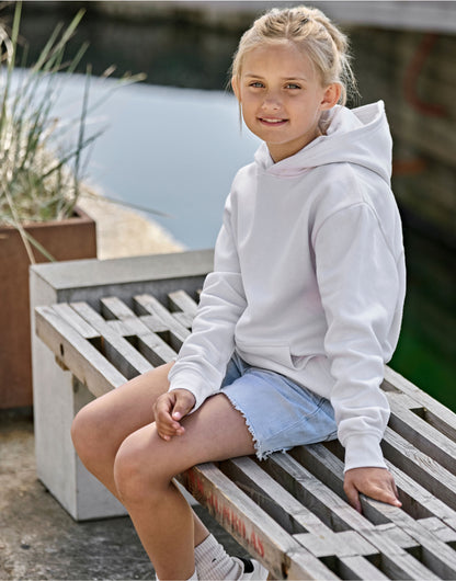 Girl wearing the Tee Jays Junior Unlabelled Hooded Sweatshirt in White, sitting on a bench outdoors