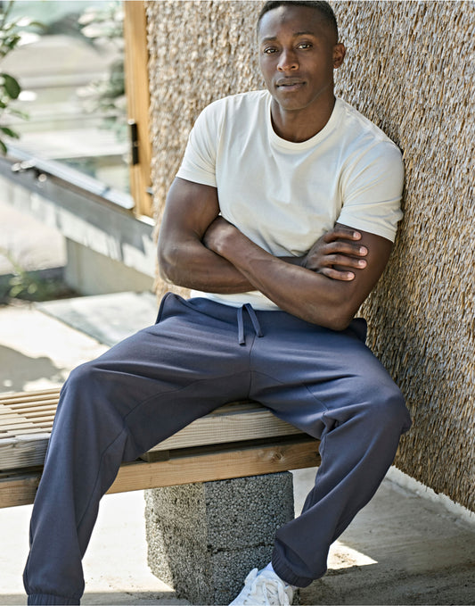 Man wearing the Tee Jays Unlabelled Sweatpants in Ink, sitting on a bench with his arms folded