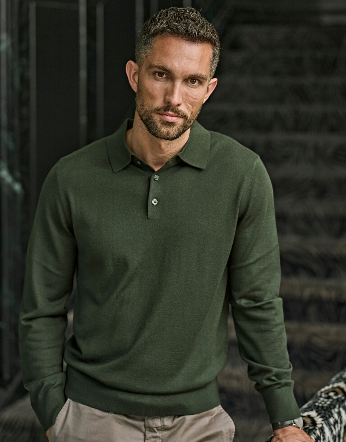 Man wearing the Tee Jays Men’s Knit Polo Shirt in Pine, standing by a stone wall