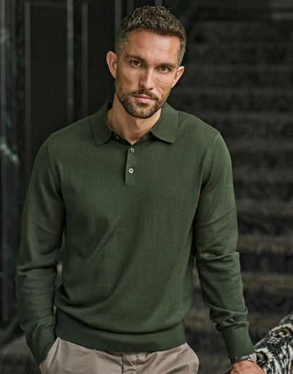 Man wearing the Tee Jays Men’s Knit Polo Shirt in Pine, standing by a stone wall