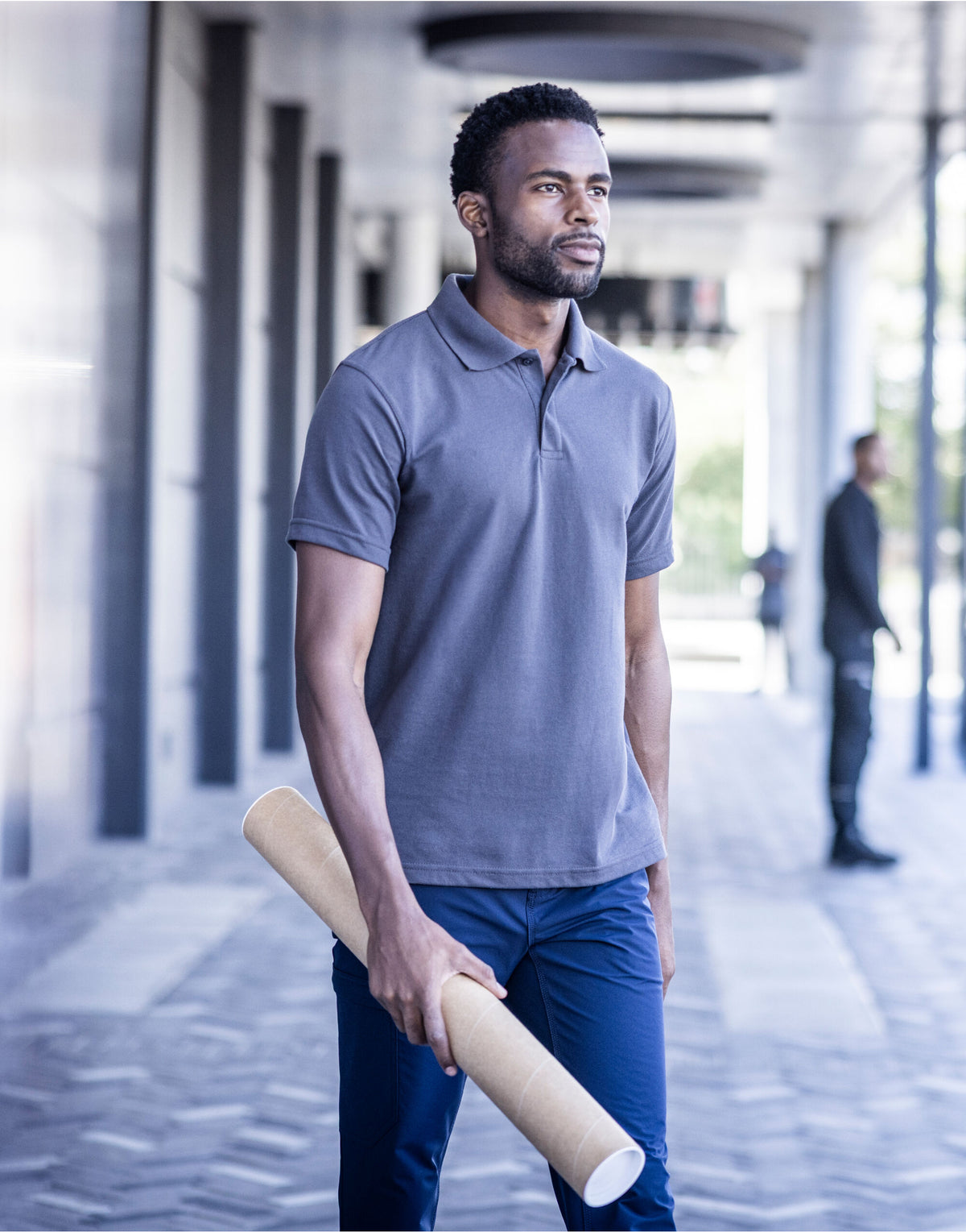 Man wearing the Regatta Pro Men’s 50/50 Pique Polo Shirt, carrying rolled-up plans under a colonnade