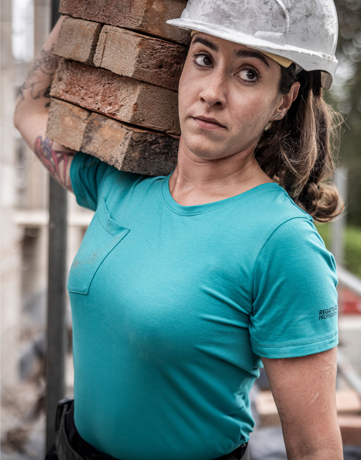 Woman in a hard hat wearing the Regatta Ada Ladies Cotton Stretch T-Shirt in Wilderness Green, carrying bricks